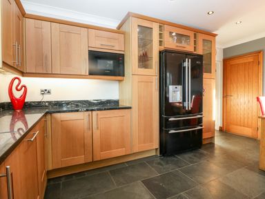 A kitchen with wooden cabinets black marble countertops a black refrigerator and a microwave at Tyn Rallt Ice Cream Farm Malltraeth near Newborough