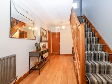 A hallway with wooden flooring staircase with striped carpet and a console table with a lamp and elephant statue at Tyn Rallt Ice Cream Farm Malltraeth near Newborough