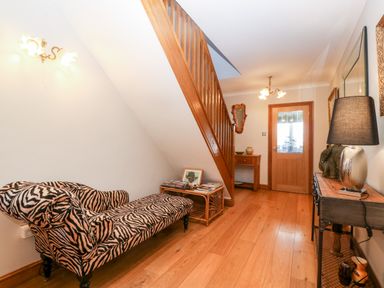 A hallway with a wooden staircase zebra print chaise lounge wooden floor a small table and a sideboard with a lamp at Tyn Rallt Ice Cream Farm Malltraeth near Newborough