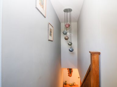 A staircase with wooden railing picture frames on a wall and a hanging light fixture with spherical shades at Tyn Rallt Ice Cream Farm in Malltraeth near Newborough
