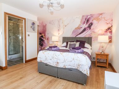 A bedroom with a bed with purple and white bedding two bedside tables with lamps and an en suite bathroom at Tyn Rallt Ice Cream Farm Malltraeth near Newborough