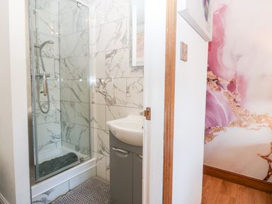 A bathroom with a glass shower enclosure a sink with cabinet and marble patterned wall tiles at Tyn Rallt Ice Cream Farm Malltraeth near Newborough