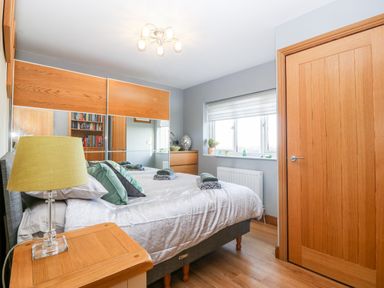 A bedroom with a bed and pillows beside a wooden door with a window on the wall at Tyn Rallt Ice Cream Farm in Malltraeth near Newborough