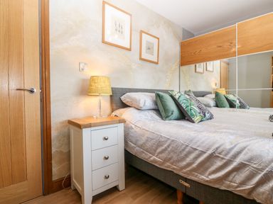 A bedroom with a bed with pillows and a bedside table with a lamp and a wooden door at Tyn Rallt Ice Cream Farm Malltraeth near Newborough