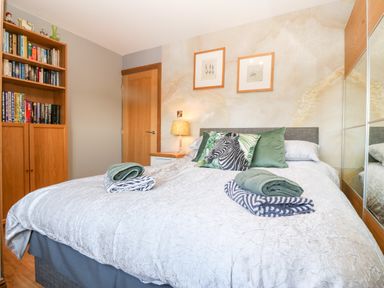 A bedroom with a double bed, two framed pictures above the bed, a bedside table with a lamp, a wooden bookshelf, and a mirrored wardrobe at Tyn Rallt Ice Cream Farm Malltraeth near Newborough