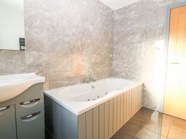A bathroom with a bathtub next to a sink cabinet and a wooden door at Tyn Rallt Ice Cream Farm in Malltraeth near Newborough