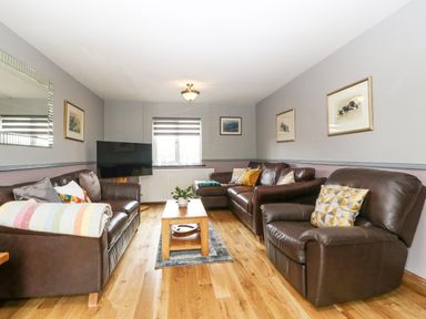 A living room with brown leather sofas a wooden coffee table a television and framed pictures on the walls at Tyn Rallt Ice Cream Farm Malltraeth near Newborough