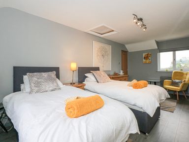 A bedroom with two single beds with white bedding and orange towels a yellow chair and a window at Tyn Rallt Ice Cream Farm Malltraeth near Newborough