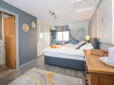 A bedroom with two single beds a window with blue and gold wall art a wooden dresser and a rug at Tyn Rallt Ice Cream Farm Malltraeth near Newborough