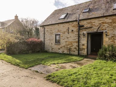 A stone cottage with a tiled roof and grassy yard at Well Cottage in Moreton-In-Marsh