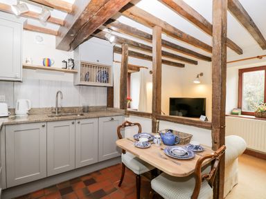 A kitchen with grey cabinets a wooden dining table set with blue and white dishes and wooden beams at Well Cottage in Moreton-In-Marsh