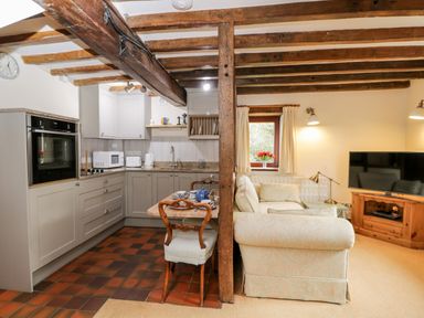 A combined kitchen and living area with wooden beams and a small dining table at Well Cottage in Moreton-In-Marsh