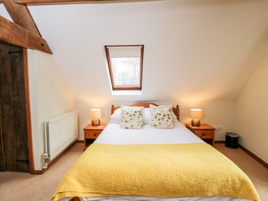A bedroom with a bed with yellow blanket and floral pillows two bedside tables with lamps and a skylight window at Well Cottage Moreton-In-Marsh