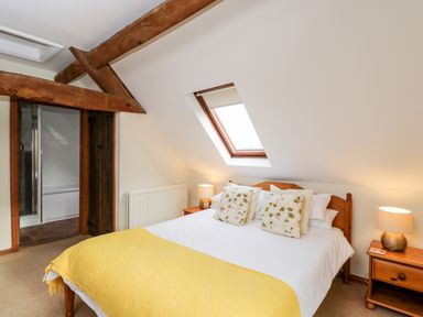 A bedroom with a double bed with floral pillows and a yellow throw under a skylight window at Well Cottage in Moreton-In-Marsh