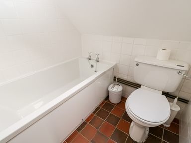 A bathroom with a white bathtub toilet small trash bin and toilet brush at Well Cottage in Moreton-In-Marsh