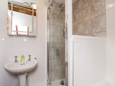 A bathroom with a sink and mirror next to a glass shower enclosure with patterned tiles at Well Cottage in Moreton-In-Marsh