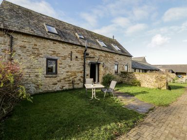 An outdoor area with a stone building a table and two chairs on grass at Well Cottage in Moreton-In-Marsh