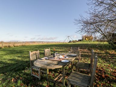 An outdoor wooden dining table with six chairs set on grass with wine glasses and a bottle at Well Cottage in Moreton-In-Marsh