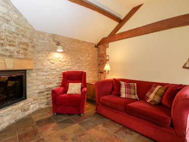 A living room with a red sofa and armchair beside a stone fireplace at Stable Cottage in Moreton-In-Marsh