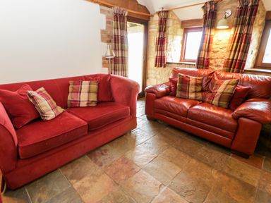 A sitting area with two red sofas and plaid cushions near windows with plaid curtains at Stable Cottage in Moreton-In-Marsh