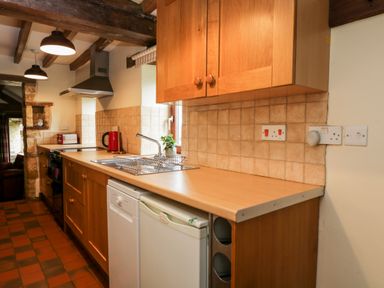 A kitchen with wooden cabinets a sink a dishwasher a mini fridge and a stove at Stable Cottage in Moreton-In-Marsh