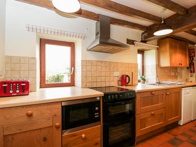A kitchen with a black oven microwave red toaster red kettle wooden cabinets and two windows at Stable Cottage in Moreton-In-Marsh