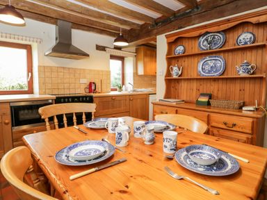 A kitchen with a wooden dining table set with blue and white patterned dishes and mugs at Stable Cottage in Moreton-In-Marsh