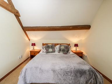 A bedroom with a double bed two bedside tables with lamps and wooden beams on the ceiling at Stable Cottage in Moreton-In-Marsh