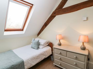 A bedroom with a single bed near a skylight window and a chest of drawers with two lamps at Stable Cottage in Moreton-In-Marsh