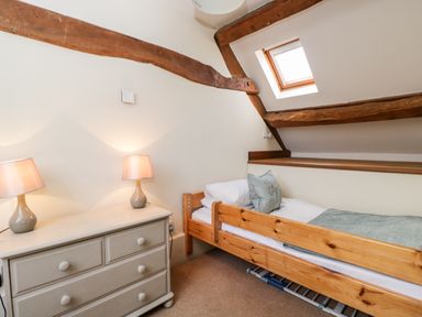 A bedroom with a wooden single bed a dresser with two lamps and exposed wooden beams at Stable Cottage in Moreton-In-Marsh