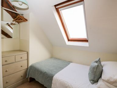 A small bedroom with a single bed under a skylight window a chest of drawers a mirror and hanging wooden hangers at Stable Cottage in Moreton-In-Marsh