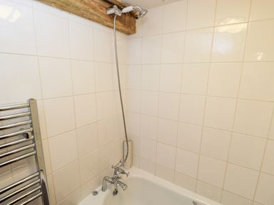 A bathroom corner with a bathtub showerhead and towel rail at Stable Cottage in Moreton In Marsh