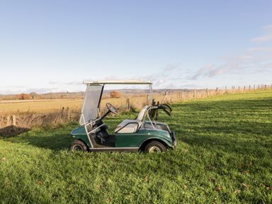 A green golf cart parked on grass with a fence and fields in the background at Stable Cottage in Moreton-In-Marsh