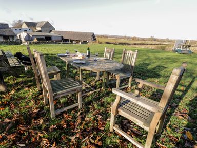 An outdoor wooden dining table with six chairs on grass with wine glasses and a bottle at Stable Cottage in Moreton-In-Marsh