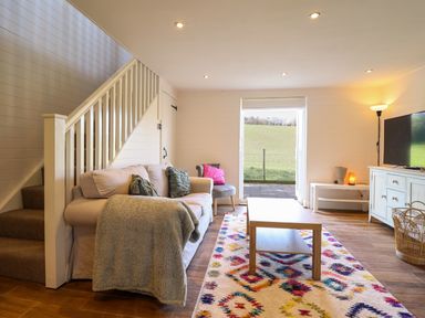 A living room with a sofa near stairs a coffee table and a television at The Stables in Tafarn-Y-Gelyn