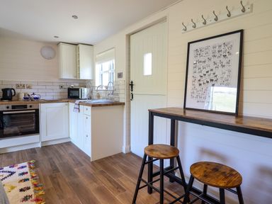 A kitchen with wooden stools a high table a door and kitchen cabinets at The Stables in Tafarn-Y-Gelyn