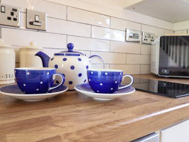 A kitchen counter with blue and white polka dot teapot and matching cups with saucers near a microwave and tiled backsplash at The Stables in Tafarn-Y-Gelyn
