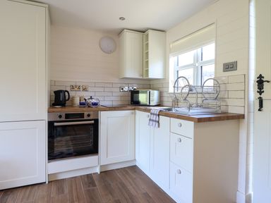A kitchen with white cabinets a wooden countertop an oven a kettle a microwave and a dish drying rack at The Stables in Tafarn-Y-Gelyn