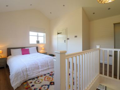 A bedroom with a bed and nightstands next to a window and white wooden railing at The Stables in Tafarn-Y-Gelyn