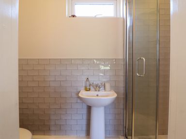 A bathroom with a pedestal sink soap dispenser toilet paper and a glass shower enclosure at The Stables in Tafarn-Y-Gelyn