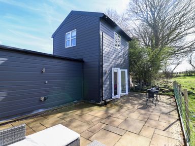 A patio area with outdoor seating and a table next to a two-story dark grey building at The Stables in Tafarn-Y-Gelyn