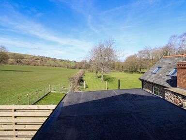 A grassy field with trees next to a stone building with a slate roof at The Stables in Tafarn-Y-Gelyn