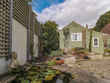 A garden with a pond and a Buddha statue next to a green wooden shed at The Potting Shed in Combe near Langport