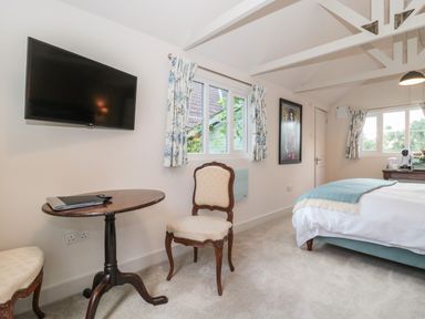 A bedroom with a wall-mounted TV a small round table two chairs and a bed with blue bedding at The Potting Shed in Combe near Langport