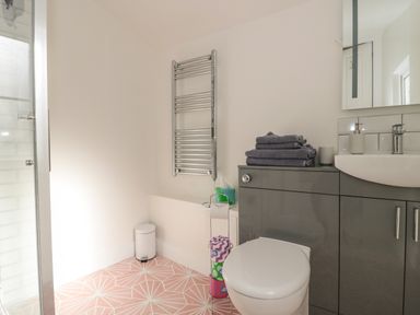 A bathroom with a toilet grey cabinets a sink towels and a heated towel rail at The Potting Shed in Combe near Langport