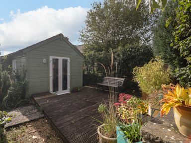 A garden with a wooden shed a bench several potted plants and trees at The Potting Shed in Combe near Langport