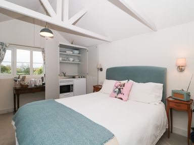 A bedroom with a bed a kitchenette and a table under a window at The Potting Shed in Combe near Langport
