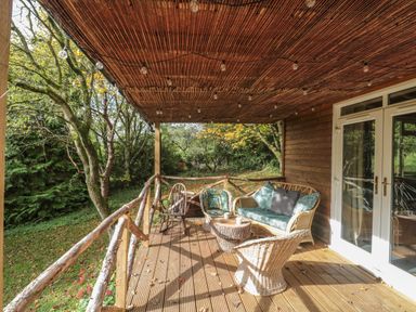 A wooden deck with wicker furniture and string lights overlooking trees at Pear Tree Lodge in Combe near Langport