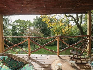 A porch with a wooden rocking chair wicker chair a wooden table with two mugs and a garden view at Pear Tree Lodge in Combe near Langport