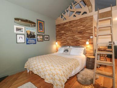 A bedroom with a double bed covered with a blanket a wooden ladder and a wall with framed pictures at Pear Tree Lodge in Combe near Langport